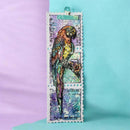 A postage stamp-style bookmark featuring a colorful parrot illustration with vintage text and a turquoise clip at the top, photographed against a split lavender and light blue background.