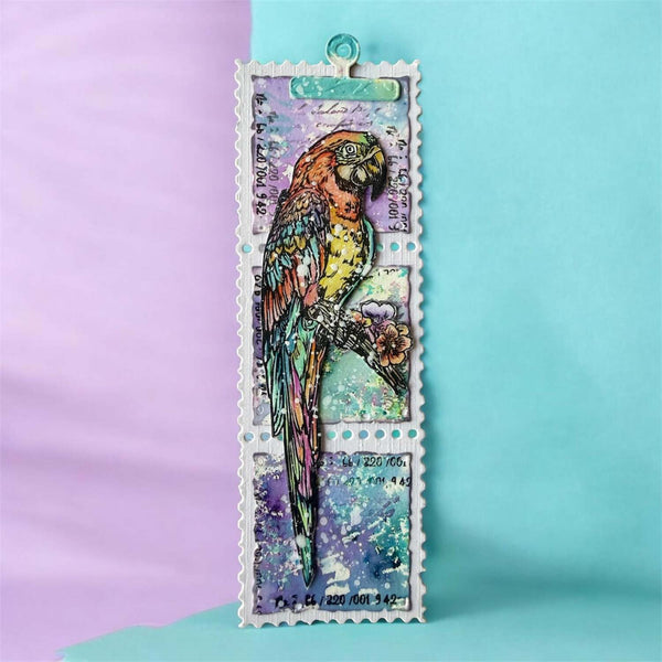 A postage stamp-style bookmark featuring a colorful parrot illustration with vintage text and a turquoise clip at the top, photographed against a split lavender and light blue background.