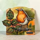 A decorative plaque or sign featuring a painted robin bird perched on a branch with green leaves, set against an autumnal orange and yellow background. The word 'Serenity' appears in a black box near the bottom right.