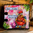 A square handmade greeting card or art print featuring a colorful illustrated rooster wearing a red and yellow striped scarf, with the text 'Happy Holidays' and 'The most wonderful time of the year.' The card has a black scalloped border and decorative green leaf accents, photographed on a rustic wooden surface.
