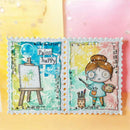 Two decorative postage-stamp-style cards or art prints shown side by side on a pastel background. The left stamp has a blue watercolor wash, an easel, and the words 'Paint happy.
