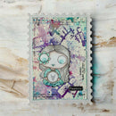 A square mixed-media art card or journaling piece featuring a stylized doll illustration, placed on a distressed white wood background. The artwork has a scalloped border, a watercolor splatter background in purple, teal, and cream, and decorative text elements.
