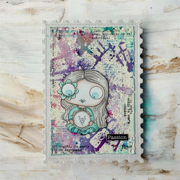 A square mixed-media art card or journaling piece featuring a stylized doll illustration, placed on a distressed white wood background. The artwork has a scalloped border, a watercolor splatter background in purple, teal, and cream, and decorative text elements.