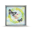 A square framed art print featuring two black and white butterflies arranged within a green leaf wreath on a pastel blue and yellow background with bubble patterns and the words 'JOY', 'smile', and 'APPRECIATE'.