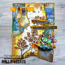 A handmade mixed-media art card featuring distressed brown and gold paper textures, two vintage lightbulb embellishments, a green cartoon frog with pink wings, and text stickers reading 'The darkest nights produce the brightest stars'.