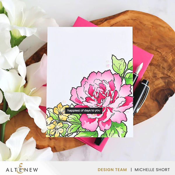 Floral card with pink flower design on a wooden surface with flowers and a pen.