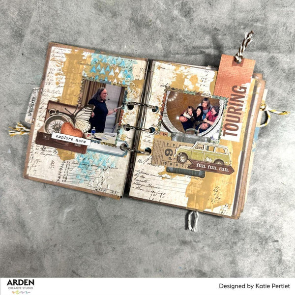 Open scrapbook with travel-themed pages on a gray surface, featuring images of people and vehicles.