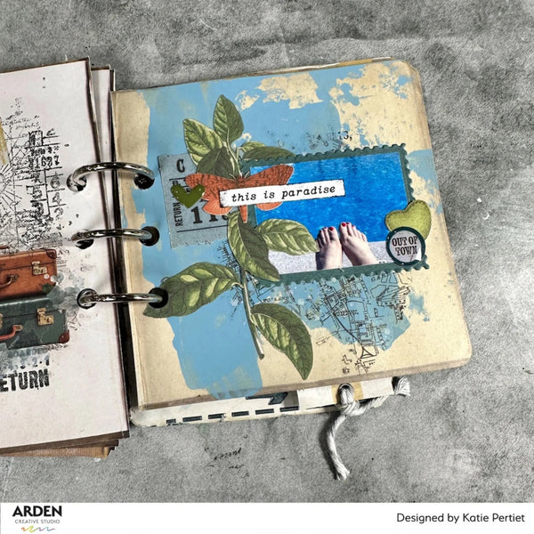 Open notebook with decorative pages featuring nature and travel-themed illustrations on a gray surface.