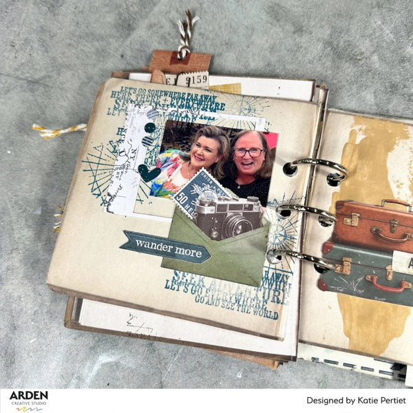 Open scrapbook with travel-themed pages on a textured surface, featuring text and images of people and travel items.