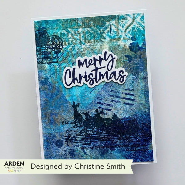 A handmade Christmas greeting card with a blue and teal abstract background, black silhouette artwork of a sleigh and deer, and the words 'Merry Christmas' in white script. The card is photographed against a light gray background with a banner at the bottom reading 'Designed by Christine Smith' and the brand 'Arden' visible in the lower-left corner.