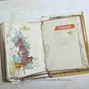 An open vintage-style mixed-media journal or scrapbook book on a light background. The pages show distressed cream paper with a map of the UK in muted blue, pink, and green tones on the left, and a cream page with a red 'FEARLESS' label, airplane sketch, and radiating lines on the right.