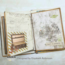An open handmade paper journal or notebook spread, showing two decorated pages with handwritten notes, stamps, collage elements, and a suitcase illustration. The pages are photographed on a light neutral background with branding text at the bottom reading 'ARDEN' and 'Designed by Elizabeth Robinson'.