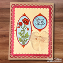 A handmade greeting card featuring a cream striped background, a pink scalloped border, a red poppy illustration in an oval frame, a circular badge with the phrase 'Blessed are the Merciful' in script, and a large beige fabric flower embellishment. The card is photographed flat on a brown wood surface.