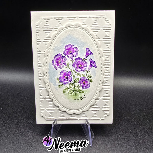 A handmade greeting card with a white embossed geometric border and a central oval illustration of purple flowers with green leaves, displayed on a clear stand against a black background.