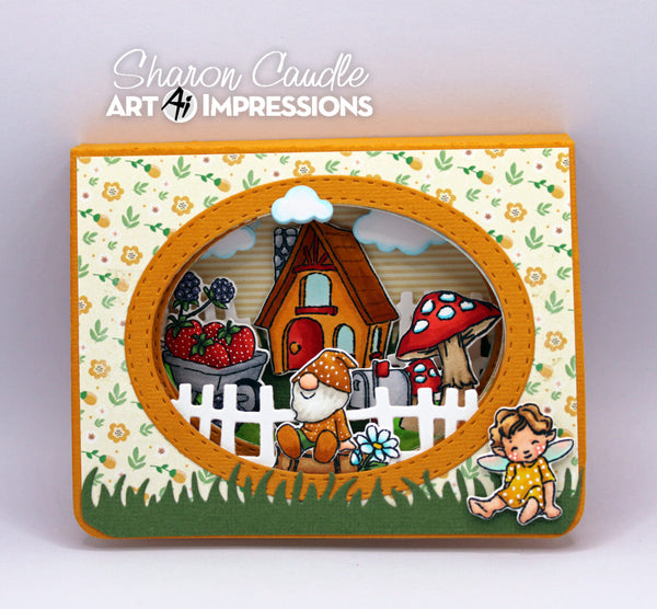 A handmade layered card or craft box featuring a whimsical garden scene with a small house, mushroom, fence, flowers, and cartoon characters. The design has a cream floral border, orange inner frame, green grass, and multicolored details.