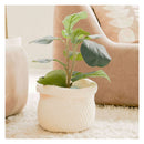 An artificial fiddle-leaf fig plant with green leaves in a cream-colored textured knit basket planter, styled on a white shag rug next to a beige armchair.