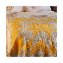 A handmade crocheted quilt with a geometric star and chevron pattern in mustard yellow and cream, styled on a bed with matching floral pillows.