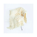 Cream-colored chunky knit throw blanket with fringe, draped over a chair on a white background.