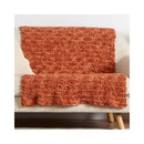 A chunky knit throw blanket in a warm rust-orange color, draped over a cream-colored sofa.
