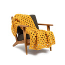 A mustard yellow crocheted throw blanket draped over a mid-century modern wooden armchair with a dark gray cushion, set against a plain white background.