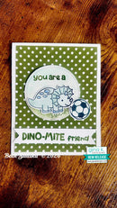 A handmade greeting card featuring a green and white polka dot background, a cute cartoon dino next to a soccer ball, and the text 'you are a DINO-MITE friend'. The card is photographed flat on a rustic wooden surface.