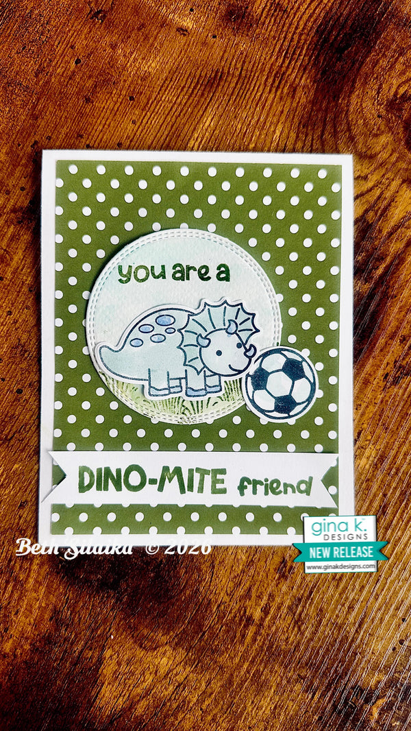 A handmade greeting card featuring a green and white polka dot background, a cute cartoon dino next to a soccer ball, and the text 'you are a DINO-MITE friend'. The card is photographed flat on a rustic wooden surface.