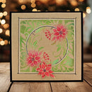A square handmade greeting card with a black border, featuring a festive holiday design with red poinsettias, green leaves, and a gold circular frame on a kraft paper background, displayed on a wooden surface with warm bokeh lights in the background.