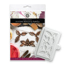 A white silicone mould with holly leaf and berry patterns, shown next to its retail packaging card by Kath Sue for Holly Corners.