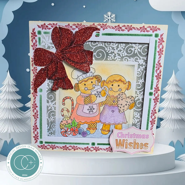 A handmade Christmas greeting card displayed on a white pedestal. The card features a large red glitter bow, a scalloped white and red border, and a central illustration of two cartoon cats wearing winter clothing, with a pink 'Christmas Wishes' tag.