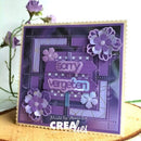 A handmade square greeting card with a purple and lavender design, featuring layered paper flowers, a central sign that reads 'sorry, vergeten', and a scalloped cream border. The card is displayed on a wooden surface with blurred purple flowers in the background.