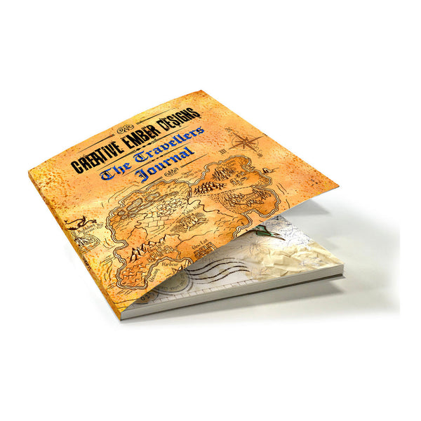 A square hardcover journal titled "The Travelers Journal" by Creative Amber Designs, featuring an antique gold map cover with blue lettering, shown open to reveal cream-colored pages underneath on a white background.