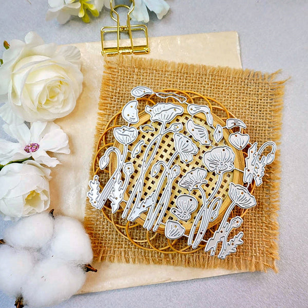 A flat-lay of a white laser-cut metal floral and botanical design sheet placed on a circular wooden coaster over a square piece of tan burlap fabric, styled with white flowers and cotton bolls on a light gray background.