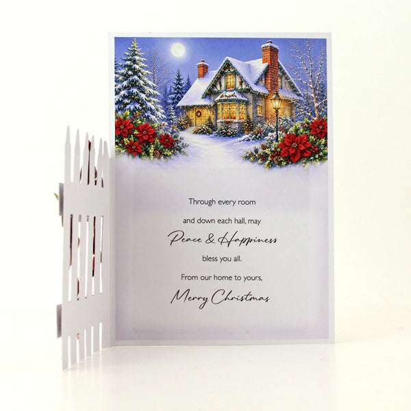 A Christmas greeting card with a winter village scene illustration and a white picket fence prop on a clean white background.