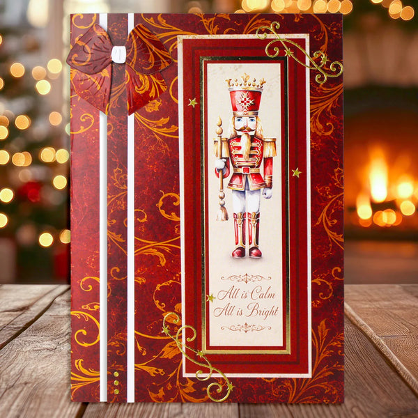 A Christmas-themed greeting card featuring a nutcracker illustration and the text 'All is Calm All is Bright,' styled on a wooden surface with a warm, blurred holiday background.