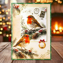 A rectangular Christmas greeting card or art print featuring two robin birds perched on snowy pine branches with vintage postage stamps and decorative flourishes. The card has a green border and is displayed upright on a wooden surface with a blurred warm holiday background.