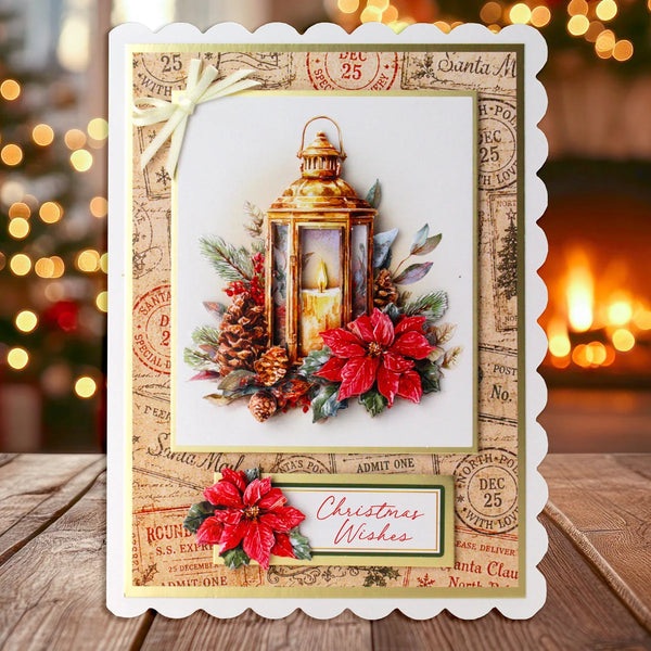 A handmade Christmas greeting card with a scalloped white border, featuring an illustration of a lantern, red poinsettias, pinecones, and vintage postage-style stamps. The card is displayed on a wooden surface with a warm, blurred holiday background.