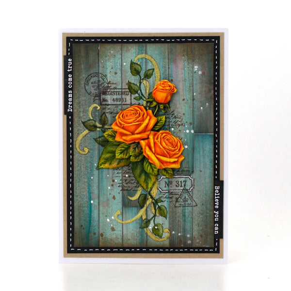 A rectangular greeting card featuring three orange roses with green leaves on a distressed teal wood-plank background, framed by a black stitched border and beige cardstock edges, photographed on a white background.