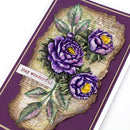 A close-up of a handmade greeting card featuring three purple peony flowers with yellow centers, green leaves, and a distressed beige paper background. The card has a deep purple border and a small white banner that reads 'stay wonderful'.