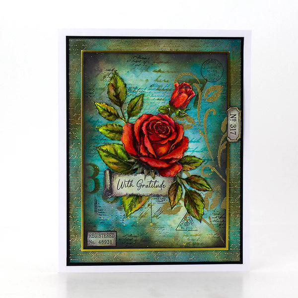 A square handmade greeting card featuring a distressed teal and gold background with two red roses, green leaves, and a banner reading 'With Gratitude'. The card is presented on a clean white background with a subtle reflection.