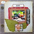 A rustic scrapbook album page featuring autumn-themed embellishments, including two olive green paper leaves, a red patterned border, a mushroom sticker, and a central photo frame with a seasonal table scene.