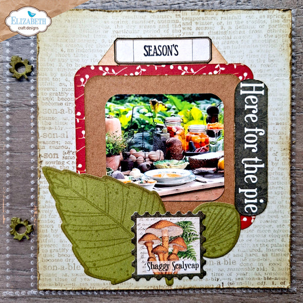 A rustic scrapbook album page featuring autumn-themed embellishments, including two olive green paper leaves, a red patterned border, a mushroom sticker, and a central photo frame with a seasonal table scene.