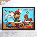 A handmade Christmas-themed card featuring a cartoon mouse dressed as an elf standing beside a small train on tracks, with a rocking horse, toy stack, and winter scene. The card is framed in black and photographed standing on a light surface.