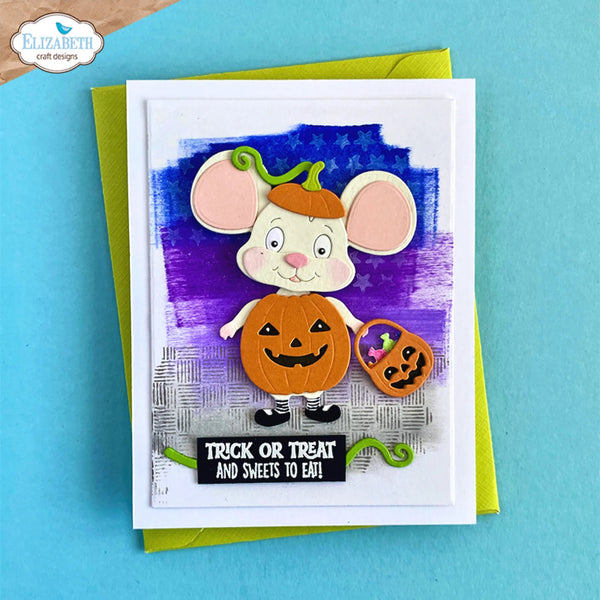A handmade Halloween greeting card featuring a cute cartoon mouse dressed as a pumpkin, holding a small bucket of treats. The card is layered over a bright yellow-green envelope and set against a solid turquoise-blue background.