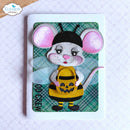 A handmade paper craft card featuring a cute mouse dressed as a bee with pink ears, a yellow and black striped body, and a jack-o'-lantern bucket. The card is displayed on a textured white surface with a wooden surface in the top-left corner.