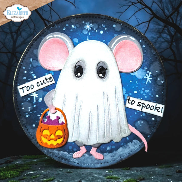 A circular Halloween-themed craft plaque or sign featuring a cute white ghost mouse with pink ears and feet, holding an orange jack-o'-lantern candy bucket. The plaque has a dark blue starry night background and is shown against a spooky outdoor scene with bare trees.