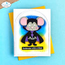 A handmade greeting card featuring a cute vampire mouse character with pink ears, a black cape, and a purple collar, set against a blue and yellow background. The card has the text 'Cuteness with a bite!' and is shown with a yellow envelope on a light blue surface.