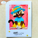 A handmade greeting card featuring a cartoon cat wearing a blue hat and bow tie against a pink background, with the text 'LOVE is a four legged word' on a light blue card border. The card is photographed on a beige fabric surface, and a 'Elizabeth craft designs' logo watermark is visible in the top-left corner.