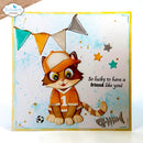 A handmade square greeting card featuring a cute cartoon cat dressed in an orange soccer jersey and cap, with colorful bunting, stars, a fish skeleton, and the text 'So lucky to have a friend like you!'. The card has a white center, a yellow border, and a blue watercolor splash background.