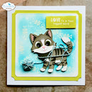A handmade greeting card featuring a 3D papercat holding a ball of yarn, set against a light blue watercolor background with fish skeleton motifs. The card has lime green borders, a white cardstock base, and a yellow sticker that reads 'LOVE is a four legged word'.