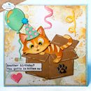 A square handmade greeting card featuring a cartoon orange kitten wearing a pink and green party hat and peeking out of a brown box. The card includes a green balloon, pink and yellow streamers, a pink heart, and the text 'Another birthday? You gotta be kitten me!'.